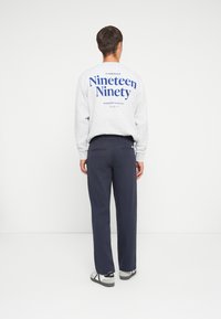 Gray sweatshirt with blue text "Nineteen Ninety" on the back, paired with dark navy pants and gray shoes with straps. Minimalist design.