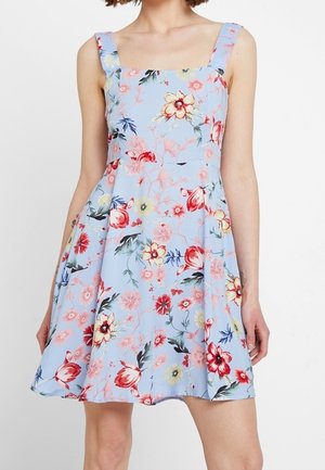 Mouwloze lichtblauwe jurk met brede bandjes en een uitlopende rok, met een meerkleurig bloemenpatroon in rood, geel, roze en groen.