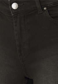 Jeans de mezclilla negra de cintura alta, con cierre de botón de metal, detalles de costura sutiles y una textura suave.