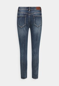 Jeans skinny de color azul oscuro, fabricados en denim. Presentan una cintura alta, cinco bolsillos y un parche de cuero marrón en la parte posterior de la cinturilla.