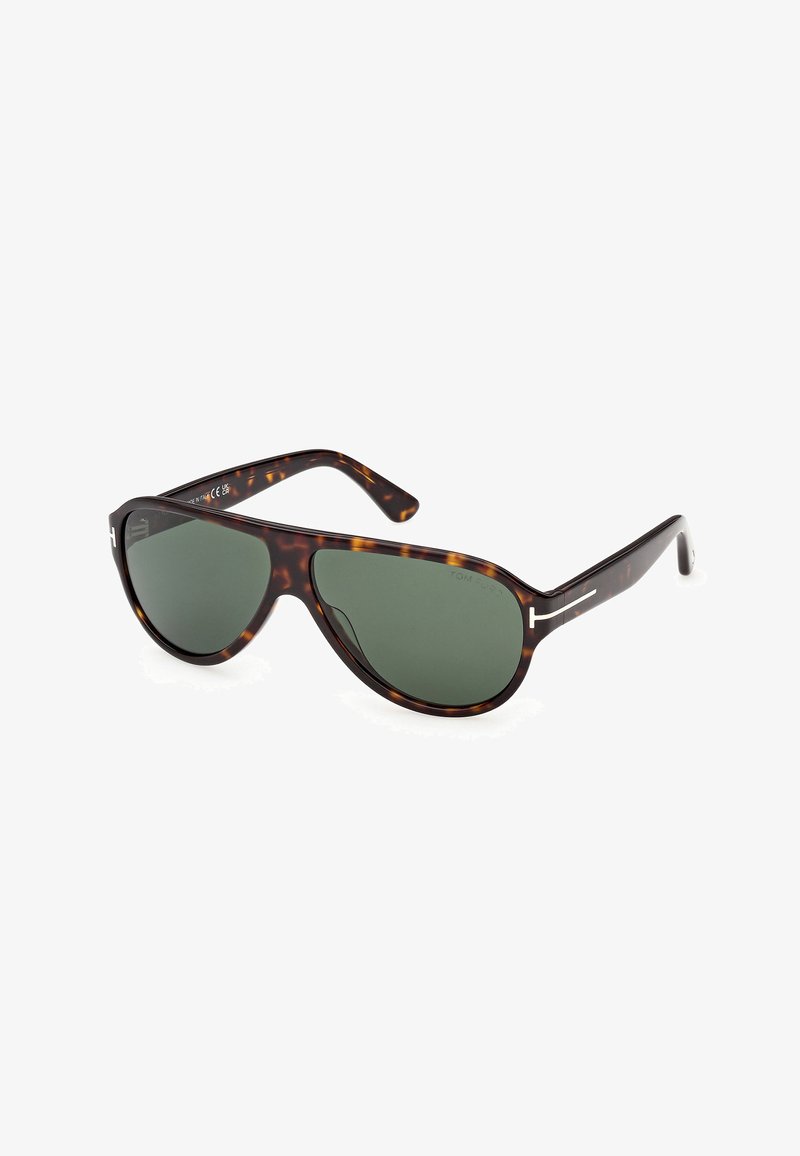 Lunettes de soleil à monture écaille avec verres vert foncé et accents de logo "T" argenté sur les branches, inclinées sur fond blanc.