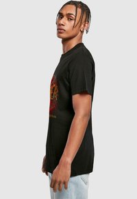 Black cotton t-shirt featuring a graphic design in red and yellow, short sleeves, and a relaxed fit, displayed from the side.