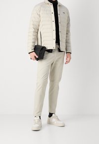 Ljust beige puffjacka, svart polotröja, krämfärgade smalna byxor och vita basketskor med beige detaljer. Svart axelväska med dragkedja.