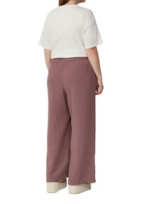 Witte, relaxte t-shirt gecombineerd met losse, gestructureerde mauve broek met een elastische taille en wijde pijpen, gedragen met beige platform schoenen.