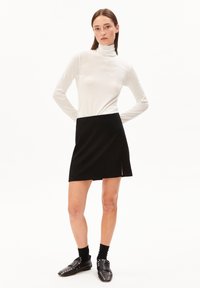 Witte coltrui gecombineerd met een zwarte mini-jurk met een zijsplit, aangevuld met zwarte loafers met zilveren studs.