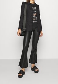 Czarna marynarka, czarny t-shirt z nadrukiem, błyszczące czarne rozszerzane spodnie oraz czarne sandały na platformie z paskami w paski. Prosta torebka na ramię.