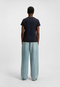 Laadun sininen t-paita lyhyillä hihoilla yhdistettynä vaaleansinisiin levyjalkaisiin farkkuihin, joissa on repaleinen helma ja ompelutiedot takataskuissa.