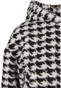 Jachetă fleece în alb și negru cu model pied-de-poule, guler înalt și material moale, texturat.