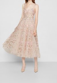 Vestido de tul beige claro bordado con flores, que presenta un escote redondo, tirantes anchos y una falda midi fluida con una textura en capas.