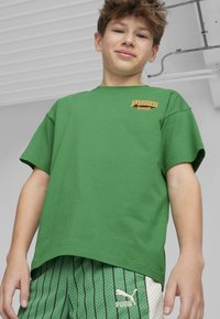 T-shirt verde in cotone con maniche corte e logo arancione. Abbinato a pantaloni corti a righe verdi con accenti bianchi e logo.