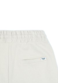 Ljusgrå joggerbyxor har ett ribbat elastiskt midjeband, en bakficka och en liten etikett med "Chelsea Peers" i blått. Mjuk textur.