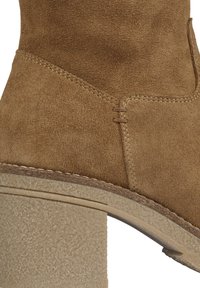 Close-up of brown suede ankle boot with visible stitching and textured beige block heel.