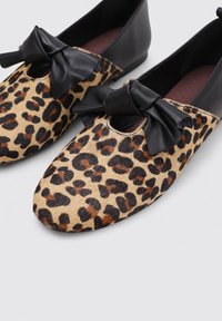 Bailarinas con estampado de leopardo y un lazo de cuero negro, con punta redondeada y superficie lisa. Material de pelo texturizado sobre cuero.