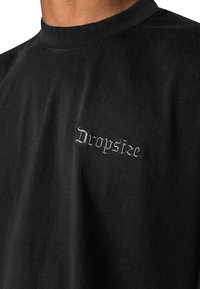 Black cotton t-shirt with a crew neck and embroidered "Dropsize" logo in gray, featuring a relaxed fit and soft texture.