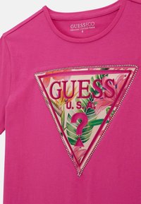 T-shirt en coton biologique rose avec un motif graphique triangulaire orné de motifs floraux, décoré de rhinestones le long des bords.