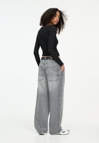 Maglietta nera a maniche lunghe abbinata a pantaloni in denim grigi oversized con grandi tasche posteriori e una cintura nera con borchie. Indossata con scarpe sportive.