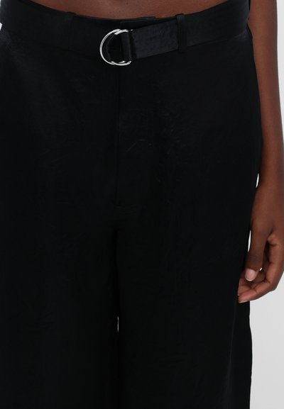 Zwarte broek met brede pijpen en een gladde textuur, voorzien van een zwarte riem met een zilveren ronde gesp en subtiele naaddetails.