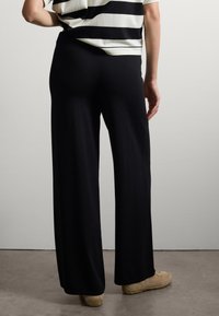 Pantalon large noir en tissu doux, doté d'une taille haute, associé à un haut rayé noir et blanc, vu de dos.