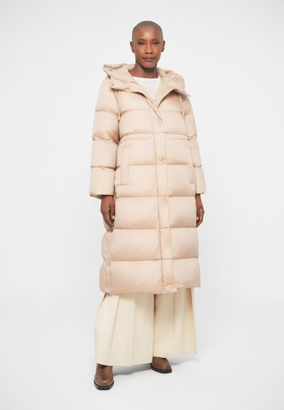 Pufi bézs hosszú kabát kapucnival, vatelin mintával, patentgombokkal és egyenes fazonnal. Széles krémszínű nadrág és barna cipő felett viselve.