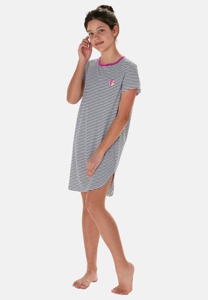 Young person standing barefoot in a short-sleeved, knee-length black and white striped dress with a pink collar and citrus patch on chest.