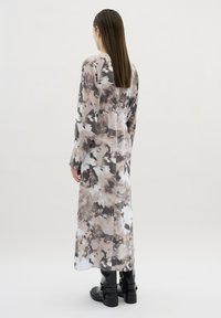 Pitkä, virtaava mekko beige ja harmaa abstrakti kuvio, jossa on istuva vyötärö ja pitkät hihat. Yhdistetty mustiin nilkkabootseihin.