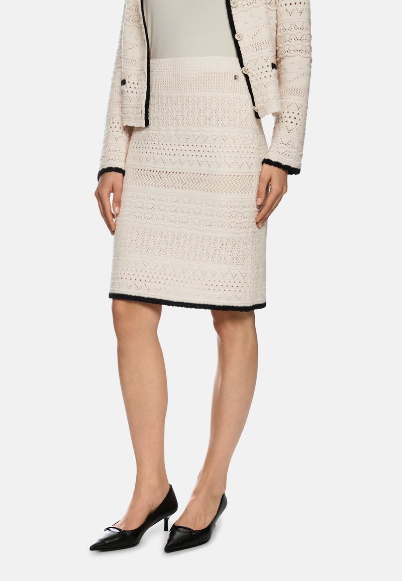 Strickrock in Creme mit strukturierten geometrischen Mustern und schwarzem Besatz; kombiniert mit schwarzen spitzen High Heels.