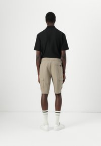 Svart kortermet polo-skjorte med liten krage, kombinert med beige cargo-shorts til kneet med sidelommer. Hvite sko og stripete sokker.