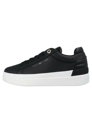 Zapatilla baja negra con suela blanca, diseño con cordones, cuello acolchado y logo de "Tommy Hilfiger" en el lateral.