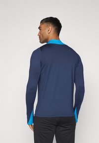 Maglietta sportiva a maniche lunghe di colore blu navy con colletto e dettagli blu brillante, caratterizzata da una vestibilità slim e cuciture piatte per il comfort.