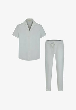Chemise blanche à manches courtes avec boutons et col, avec un pantalon blanc à cordon, disposés côte à côte sur fond blanc.