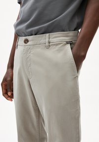 Pantaloni grigi chiari, morbidi e dal taglio comodo con una trama liscia. Presentano una chiusura a bottone e tasche laterali. Design minimalista.