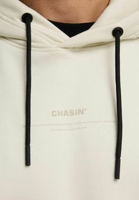 Witte hoodie met zwarte trekkoorden, voorzien van een subtiele geprinte logo "CHASIN'" op de voorkant, gemaakt van een zachte katoenmix.