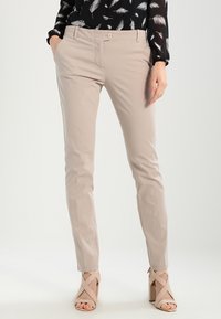Beige trousers made of smooth fabric with a slim fit, featuring a front button closure and side pockets. Paired with strappy beige heels.