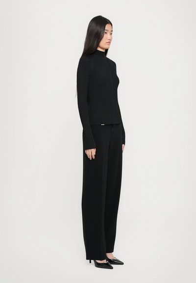 Pulover cu guler înalt, negru, cu model canelat, asortat cu pantaloni negri cu picioare largi. Aspectul are o siluetă dreaptă și mâneci lungi, completat de tocuri ascuțite.
