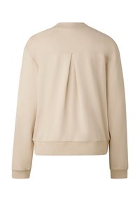 Béžová mikina s volným střihem, žebrovanými manžetami a lemem, s detailním středovým záhybem na zadní straně a hladkou texturou látky.