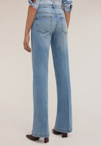 Jeans in denim azzurro chiaro a gamba svasata con vita alta, dotati di tasche posteriori e una leggera texture sbiadita. L'orlo è ampio nella parte inferiore.