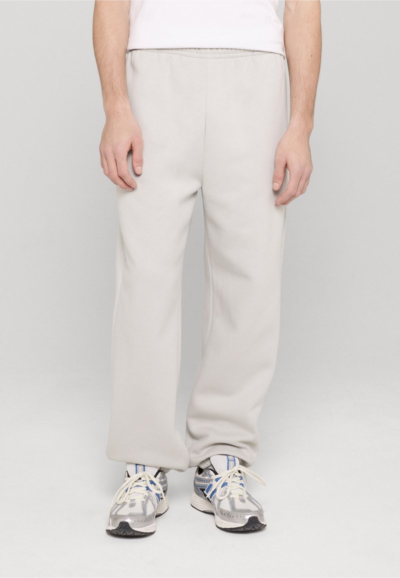 Pantaloni de trening gri deschis realizați dintr-un material moale, cu talie elastică și croială dreptă. Asortați cu pantofi sport gri și albaștri.