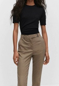 Un haut noir à manches courtes associé à un pantalon taille haute à carreaux beiges et marron, arborant une coupe ajustée et une texture lisse.