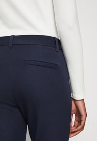 Merihenkiset housut sileästä kankaasta, slim fit -malli, litteä takatasku ja vyölenkit vyötäröllä, yhdistettynä hyvin istuvaan valkoiseen yläosaan.