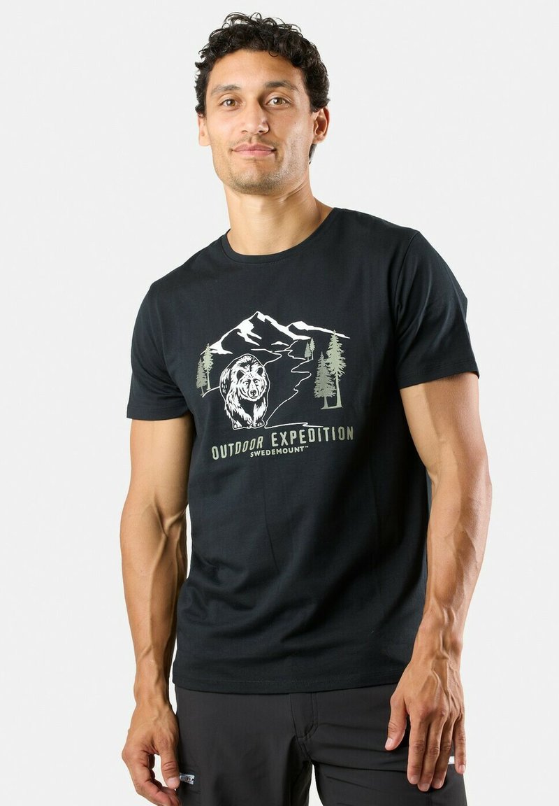 Mand iført sort t-shirt med grafik af en bjørn, træer, bjerge og teksten "Outdoor Expedition Swedemount" på forsiden.