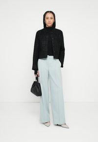 Černá texturovaná krátká bunda, přiléhavý rolák, světle modré široké kalhoty a šedé boty na podpatku se špičatou špičkou; drží malou černou tašku.