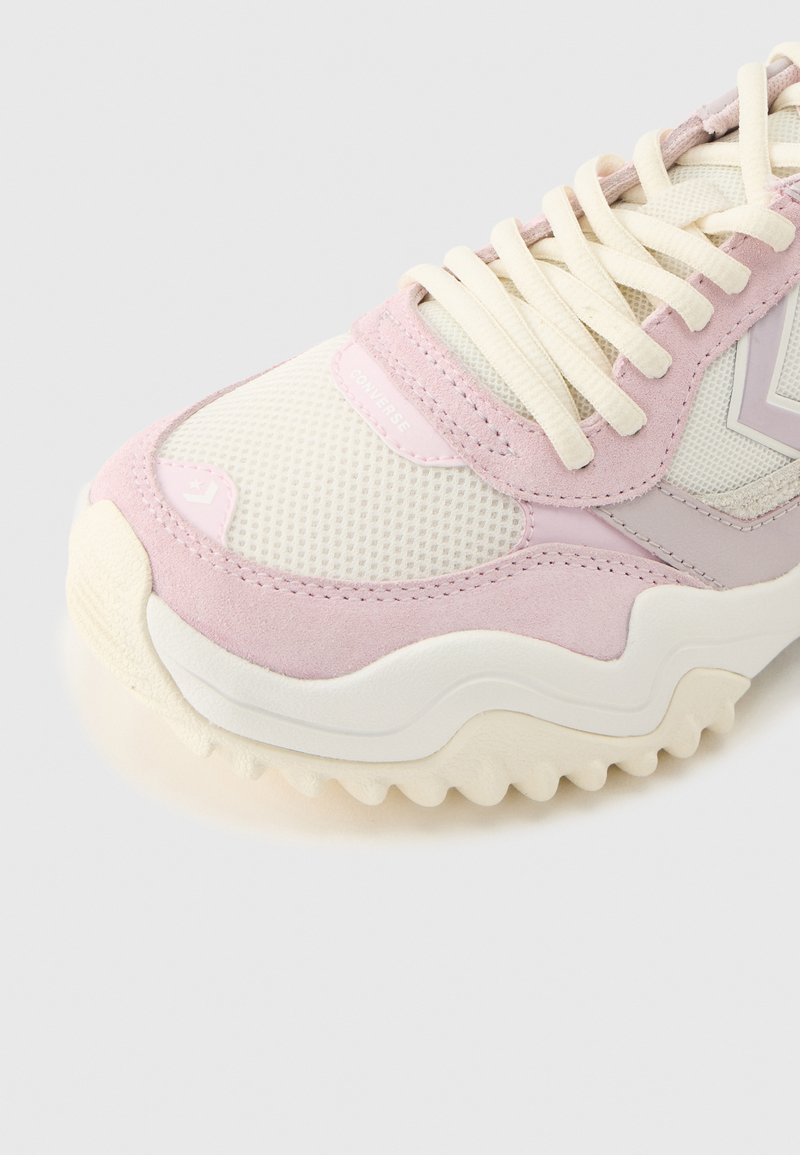 White and light pink athletic sneaker with mesh and suede textures, off-white thick sole, and white laces on a plain background.
