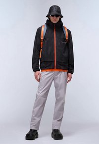 Sort jakke med orange accenter, grå bukser, sorte sko og en sort bøttehat. Outfittet har et strømlinet, moderne design og kontrasterende farver.