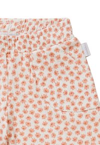 Pantalons légers en coton avec taille élastique. Fond blanc avec un petit motif floral orange. Comprend une poche latérale.