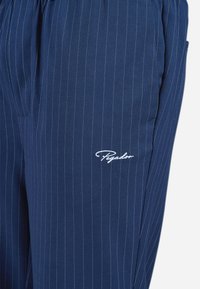 Navy broek van stof met witte streepjes. Beschikt over een geborduurd logo op de linker bovenbeen en een comfortabele pasvorm met zijzakken.