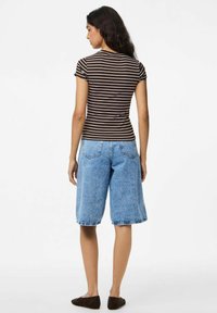 Rudas ir baltas dryžuotas trumpas rankovės marškinėliai, derinami su mėlynais džinsiniais bermudų šortais, pasižyminčiais laisvu siluetu ir apvyniotais kraštais.