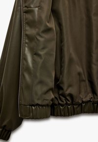 Veste bomber vert olive avec une texture lisse, des poignets élastiques et une fermeture éclair à l'avant. Présente un intérieur doublé pour plus de chaleur.