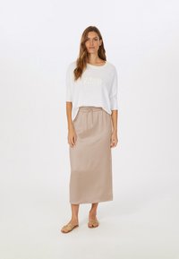 White knit sweater with "PARIS" text in textured fabric, paired with a beige satin maxi skirt featuring an elastic waistband and flat sandals.