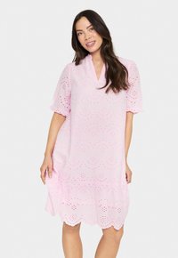 Robe en coton rose avec un décolleté en V, des manches courtes à volants et des broderies ajourées. Ourlet à volants et motifs floraux sur toute la surface.