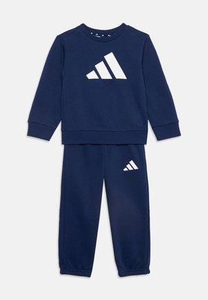 Ensemble sweat-shirt manches longues et pantalon bleu marine avec logo triangulaire blanc sur la poitrine et sur la partie supérieure de la jambe gauche, poignets élastiques aux manches et au pantalon.